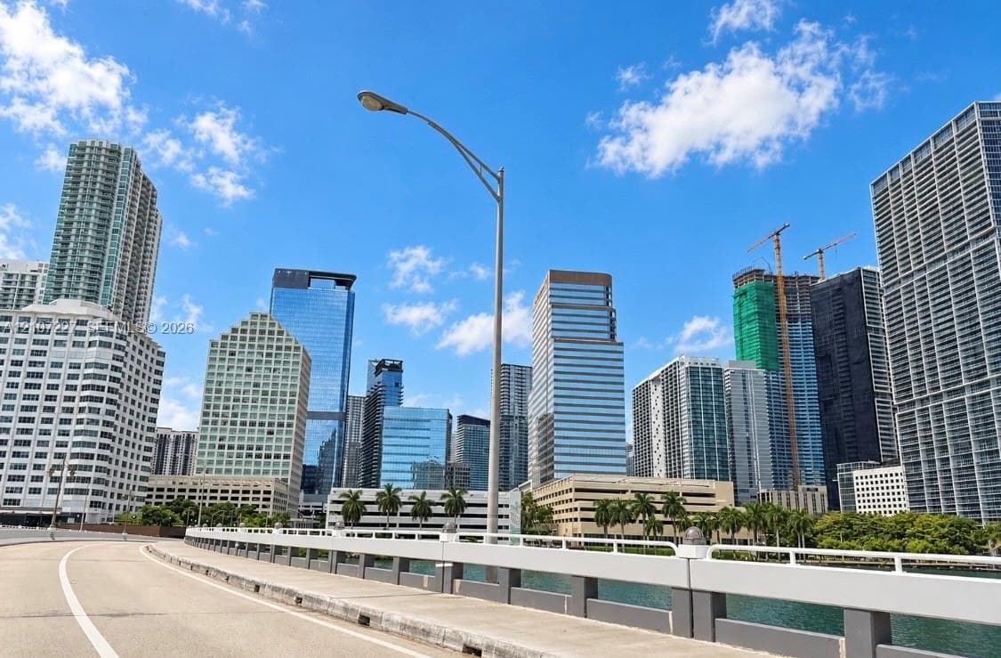 Urban landscape featuring a collection of high-rise commercial and residential towers, paved thoroughfare, and mature palm trees along the waterfront