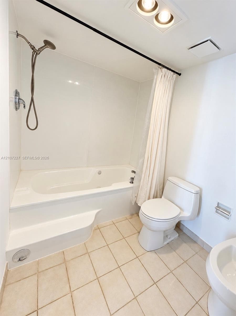 Bathroom featuring a deep soaking tub with an integrated step, an adjustable-height handheld showerhead, a seamless tub surround, and neutral tile flooring