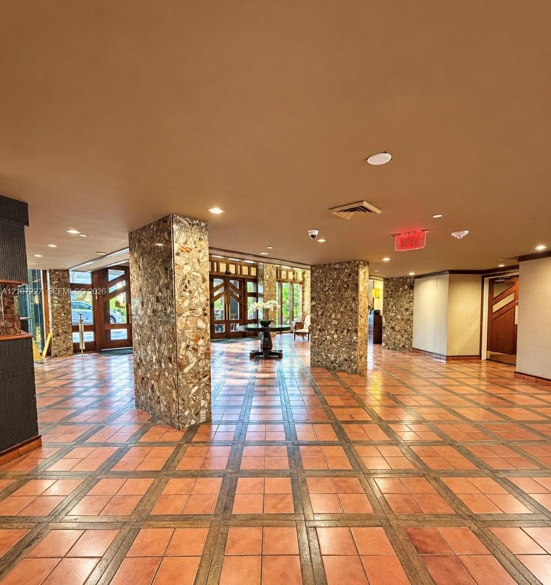 Lobby featuring terracotta tile flooring with inlay details, natural stone-clad structural pillars, recessed ceiling lighting, and multi-pane wood entry doors