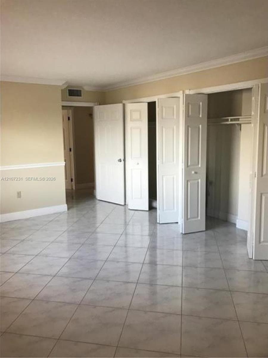 Interior space featuring light-toned tile flooring, chair rail molding, crown molding, and two sets of multi-panel closet doors