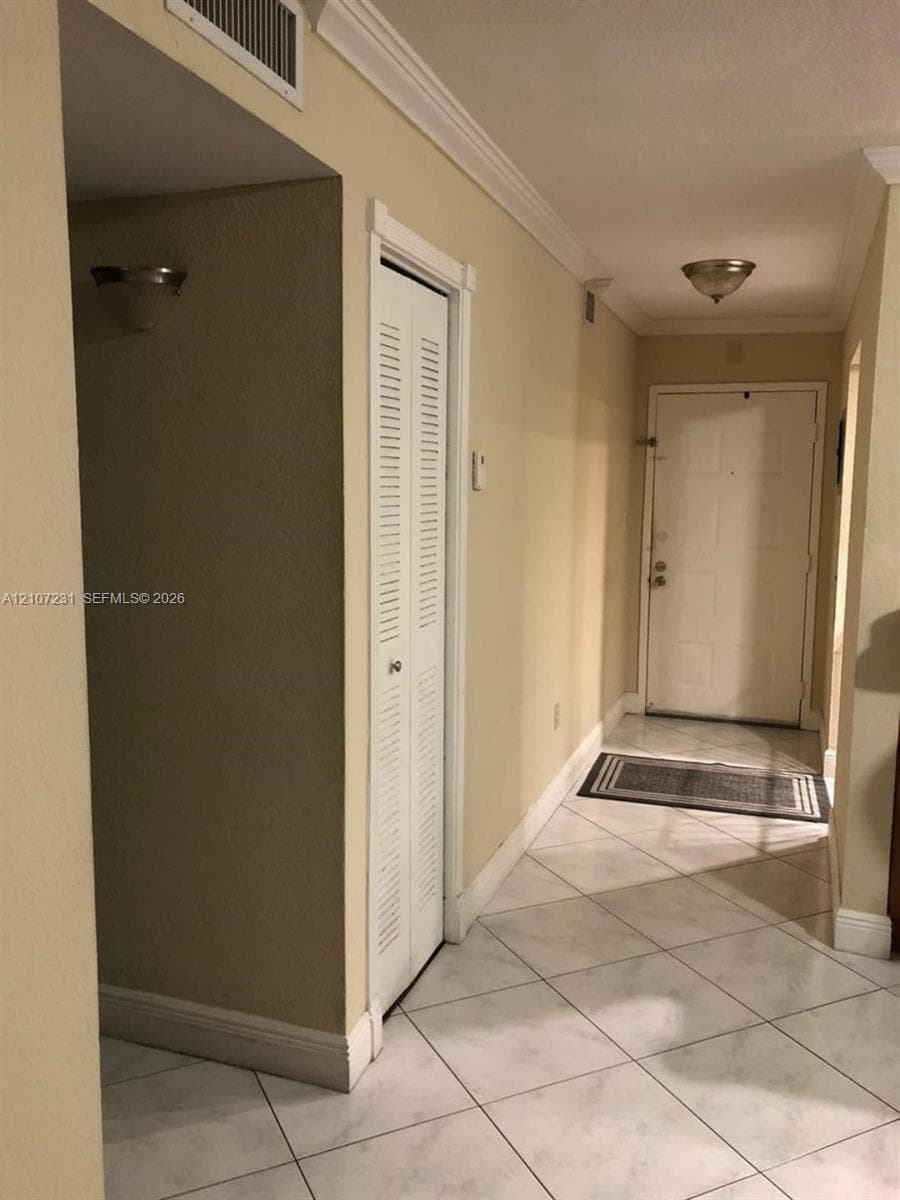 Entryway featuring diamond-patterned tile flooring, crown molding, a louvered-door closet, and overhead flush-mount lighting