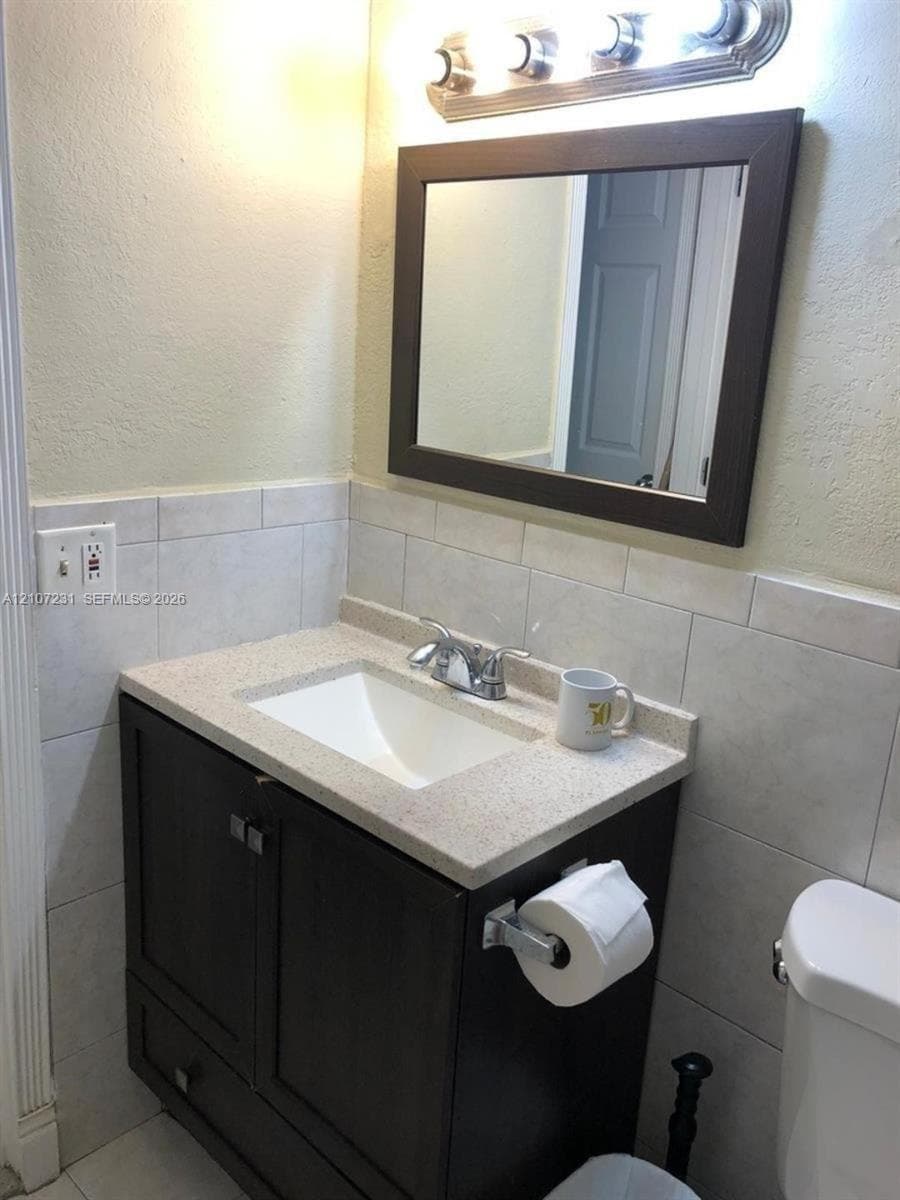 Dark wood vanity featuring a stone-composite countertop, undermount sink, ceramic tile backsplash, and a framed wall mirror