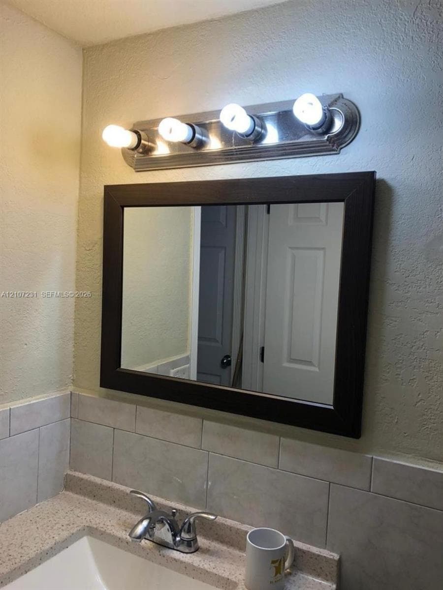 Rectangular mirror with a dark wood-finish frame, polished chrome four-light vanity fixture, integrated stone-composite countertop, and ceramic subway-style backsplash