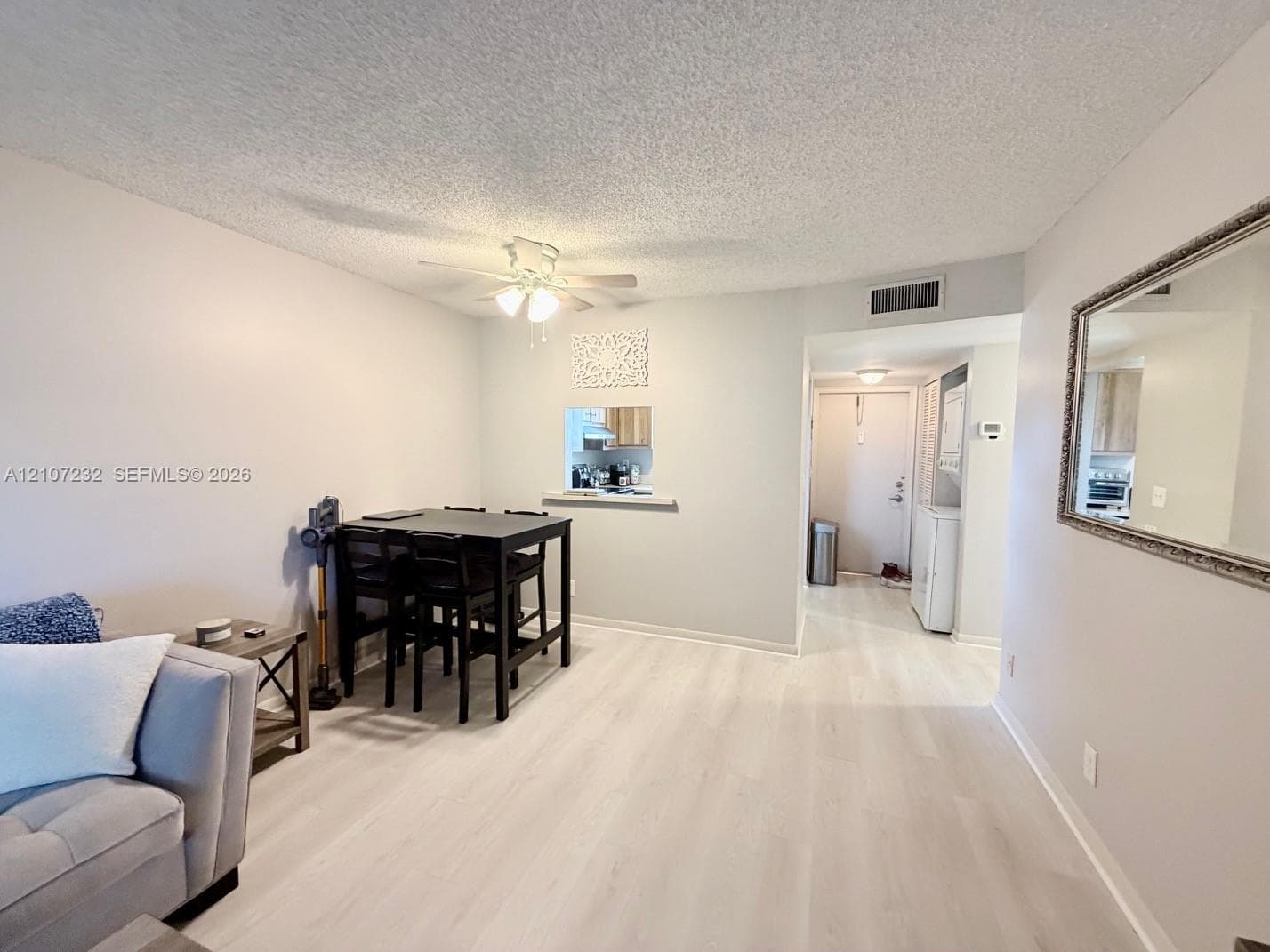 Neutral-toned interior featuring wood-finish flooring, a ceiling fan with integrated lighting, a pass-through wall opening, and a large wall-mounted mirror