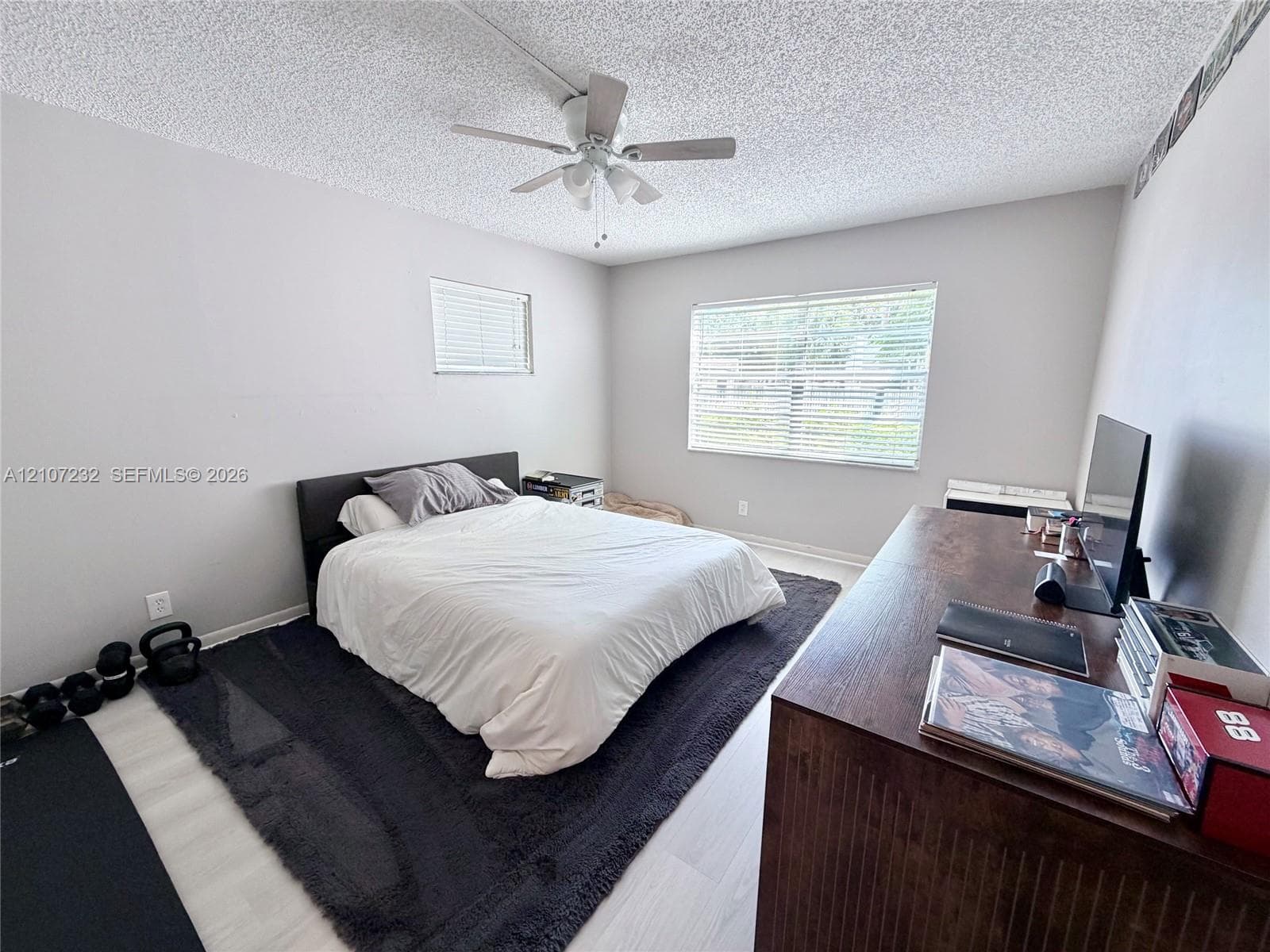 Neutral interior room featuring wood-finish flooring, a ceiling fan with integrated lighting, and dual horizontal windows with fitted blinds