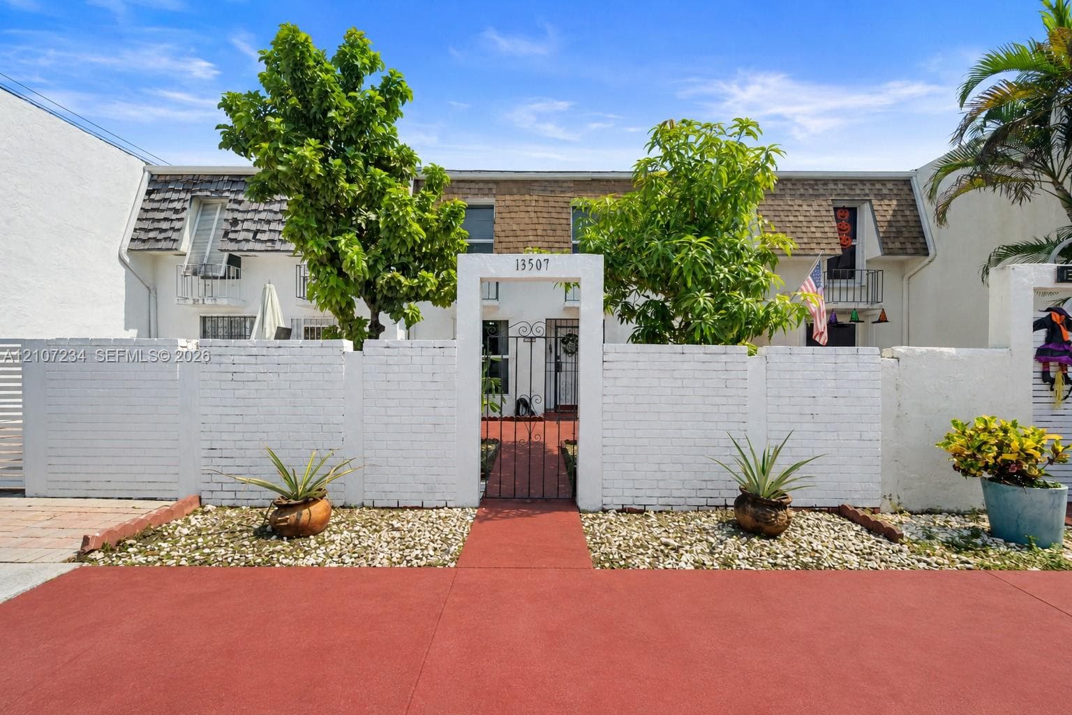 Two-story townhouse exterior featuring a white-painted brick privacy wall, a gated entryway, shingled mansard roof detailing, and individual second-story balconies