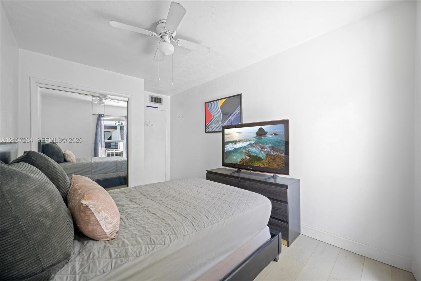 Neutral walls, wood-finish flooring, ceiling fan with integrated lighting, and dual-panel sliding mirror closet doors