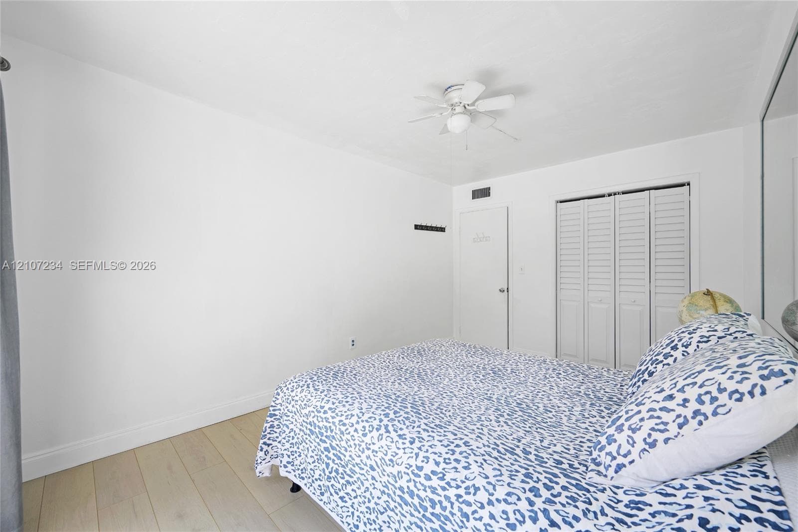 Neutral-toned wood-finish flooring, ceiling fan with integrated lighting, and white louvered bifold closet doors