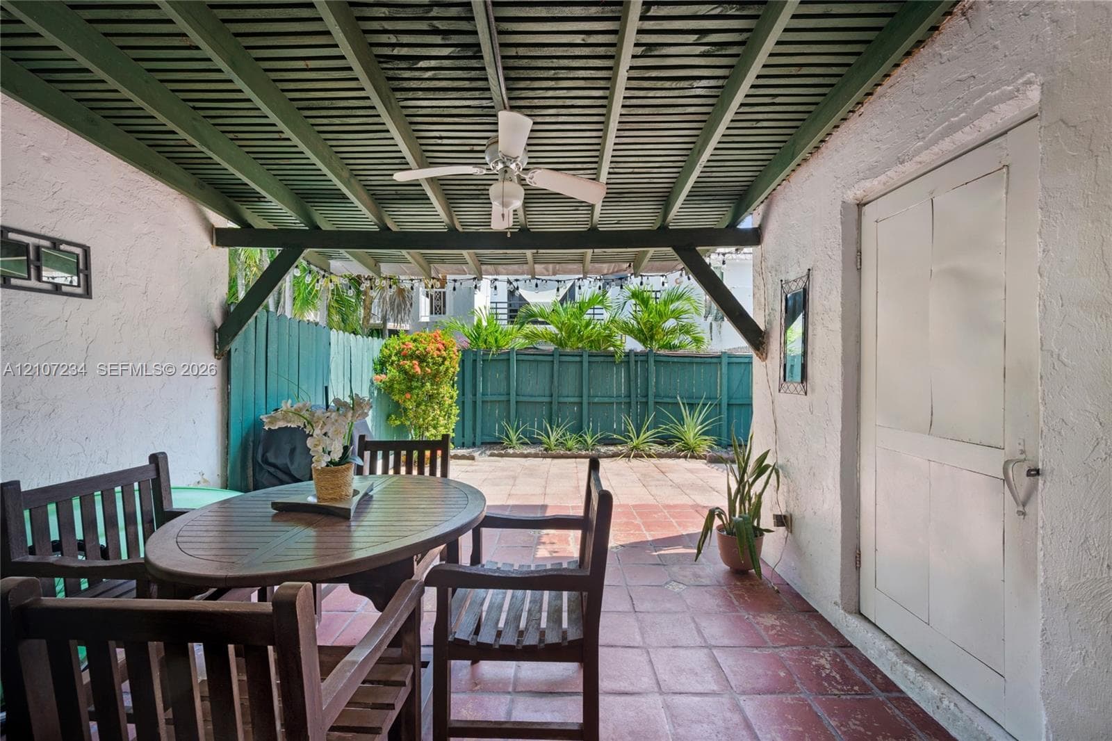 Covered patio featuring a slatted wooden ceiling with a ceiling fan, terra cotta tile flooring, stucco exterior walls, and a privacy fence