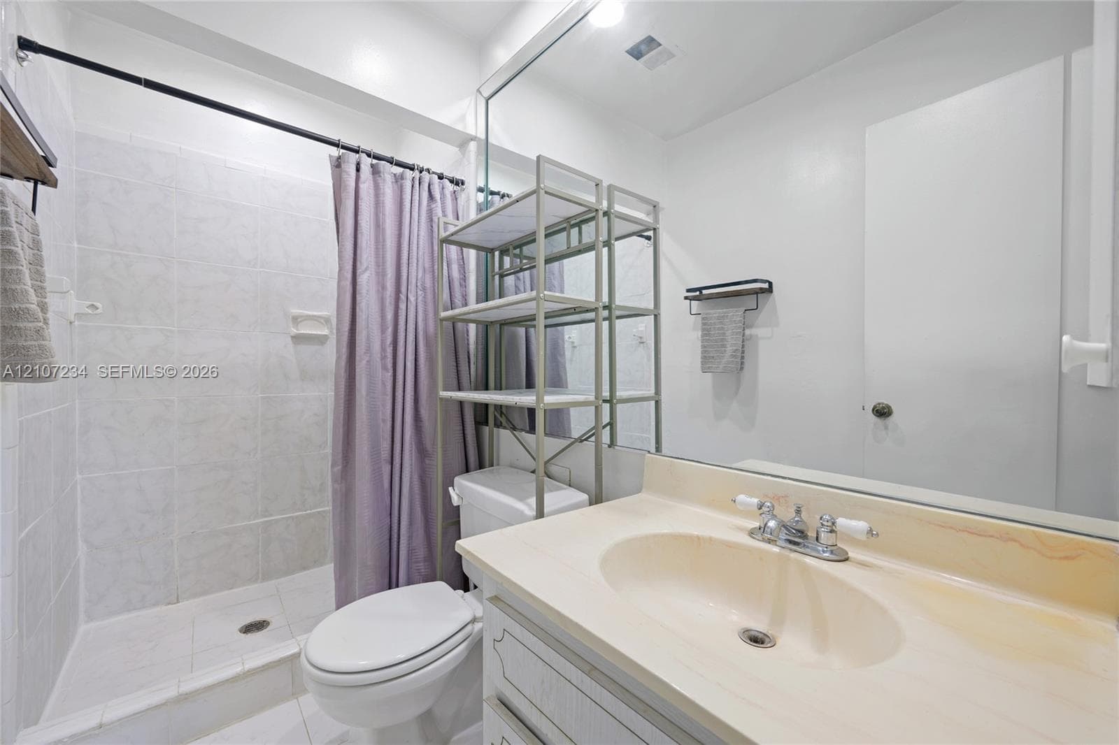 Bathroom featuring a vanity with integrated sink, expansive wall-mounted mirror, white ceramic tile shower surround, and polished chrome hardware