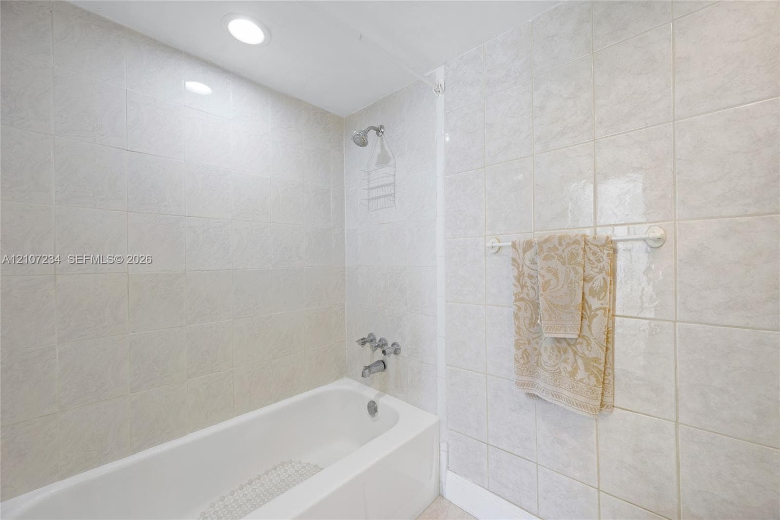 Full-height wall tiling surrounding a white bathtub with a built-in shower faucet and recessed ceiling lighting