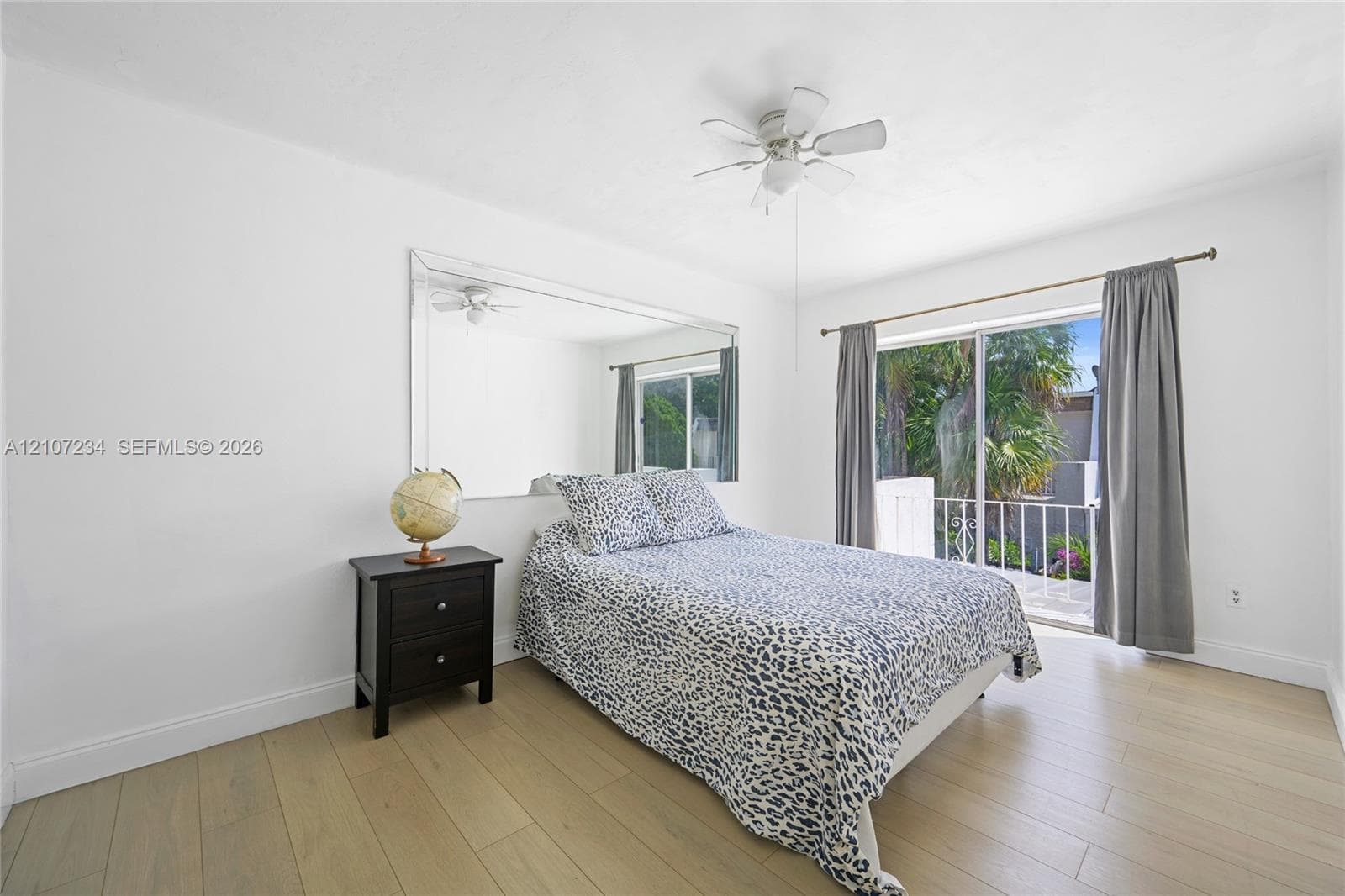 Wood-finish flooring, large wall-mounted mirror, ceiling fan with integrated light fixture, and sliding glass door with exterior railing