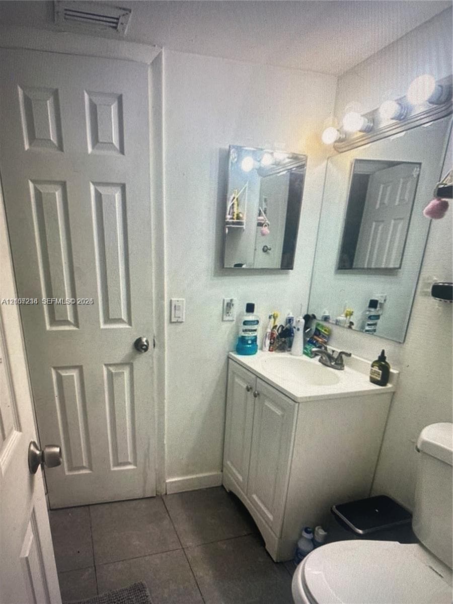 Bathroom featuring a vanity with integrated sink, chrome hardware, a wall-mounted mirror, and tile flooring