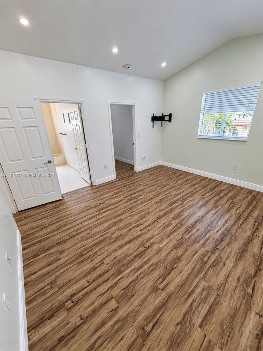 Room featuring wood-finish flooring, recessed lighting, vaulted ceilings, and a window with horizontal blinds