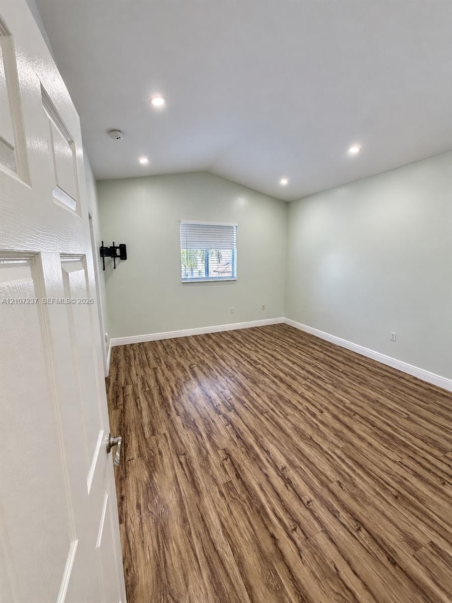 Vaulted ceilings featuring recessed lighting, wood-finish flooring, and a single window