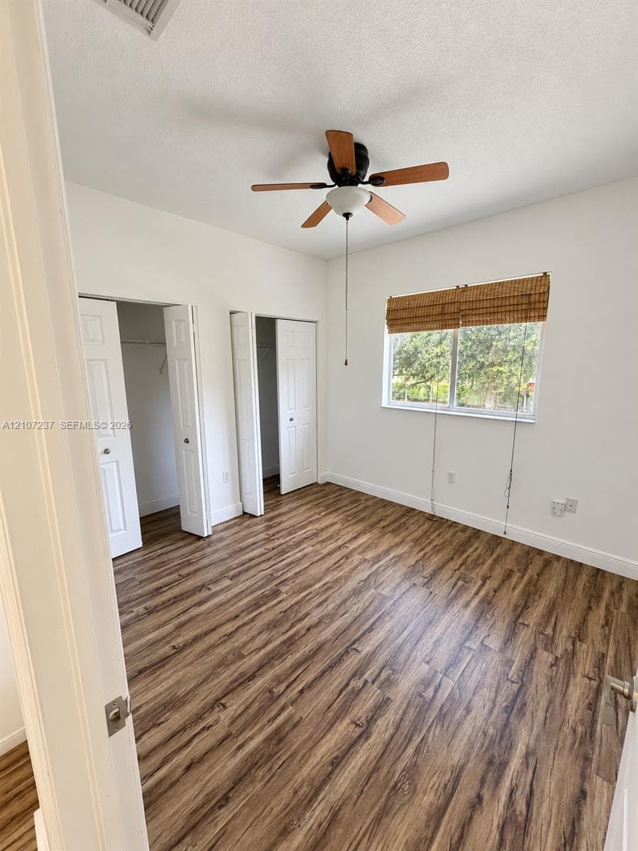 Wood-finish flooring, dual reach-in closets with panel doors, and a ceiling fan with integrated lighting