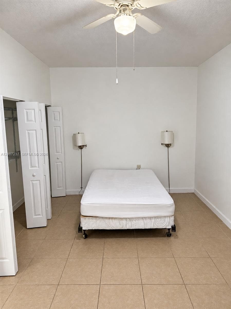 Room featuring neutral tile flooring, bi-fold closet doors, and a ceiling-mounted light fixture with a fan