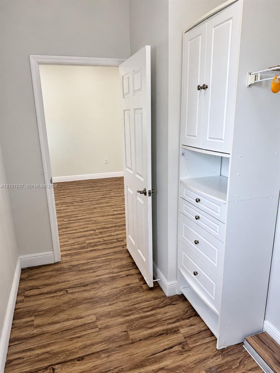 Built-in white storage cabinetry featuring shaker-style doors and multiple drawers, paired with wood-finish flooring and a six-panel door