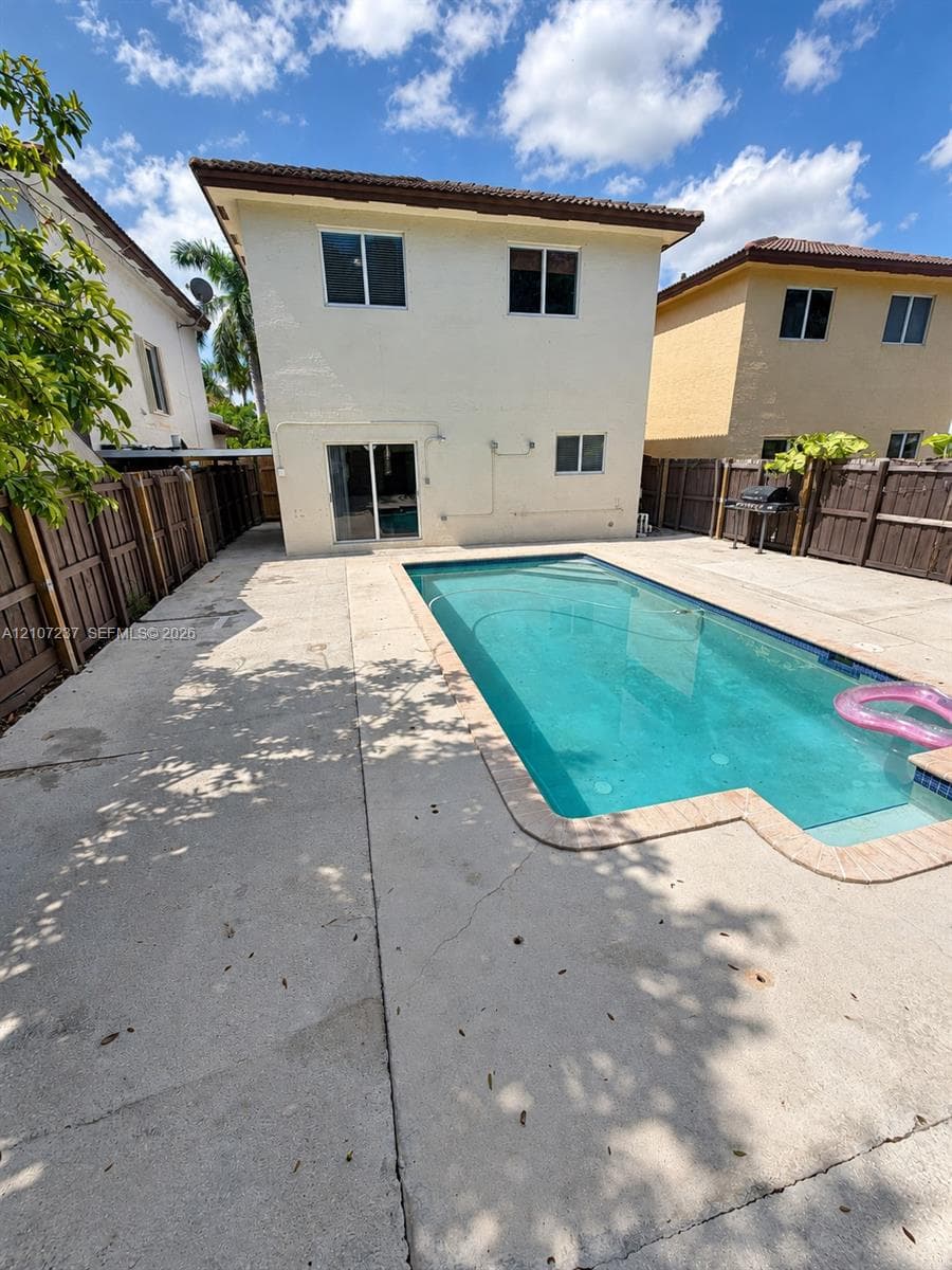 Rear exterior featuring a rectangular inground swimming pool, concrete patio, and wood privacy fencing