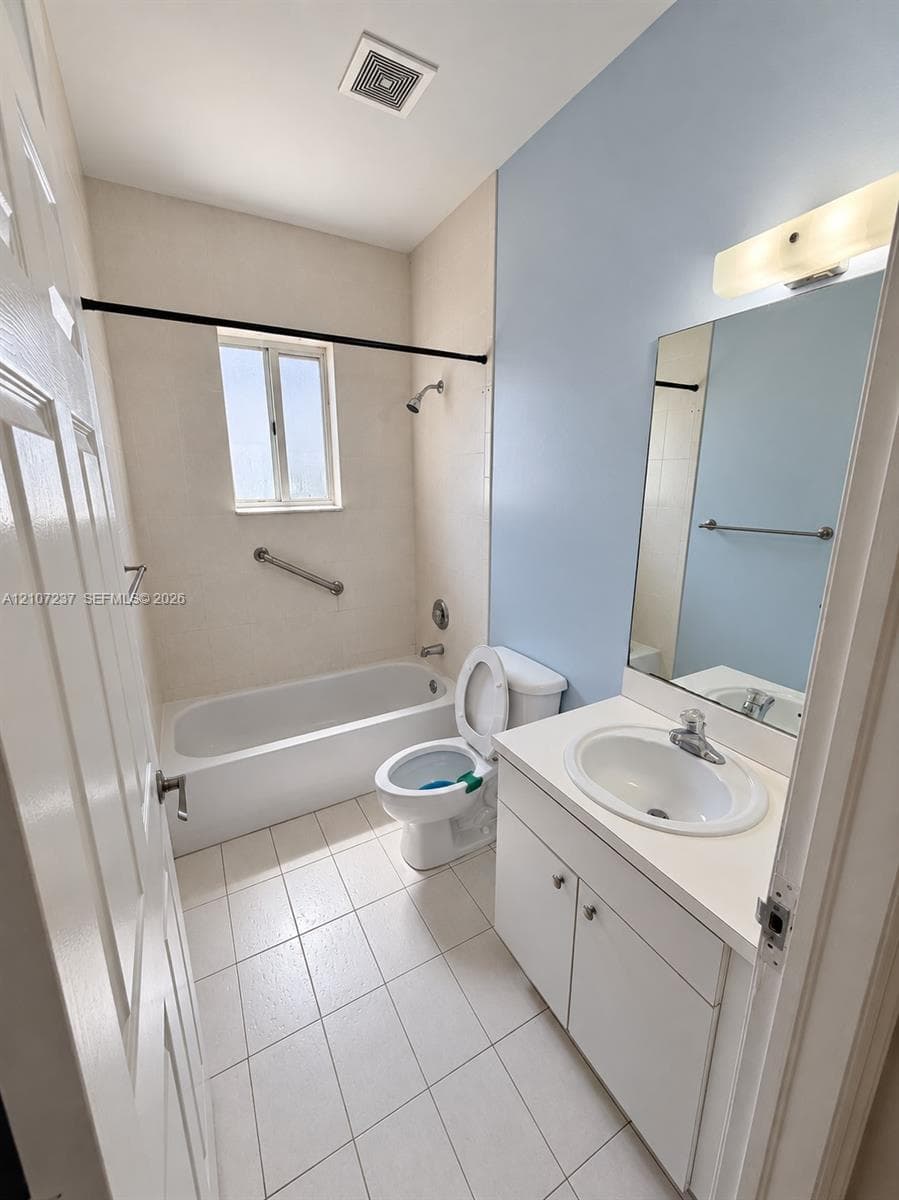 Bathroom featuring a white porcelain tub with an integrated shower, vanity cabinet with an inset sink, solid-surface countertop, and large wall-mounted mirror