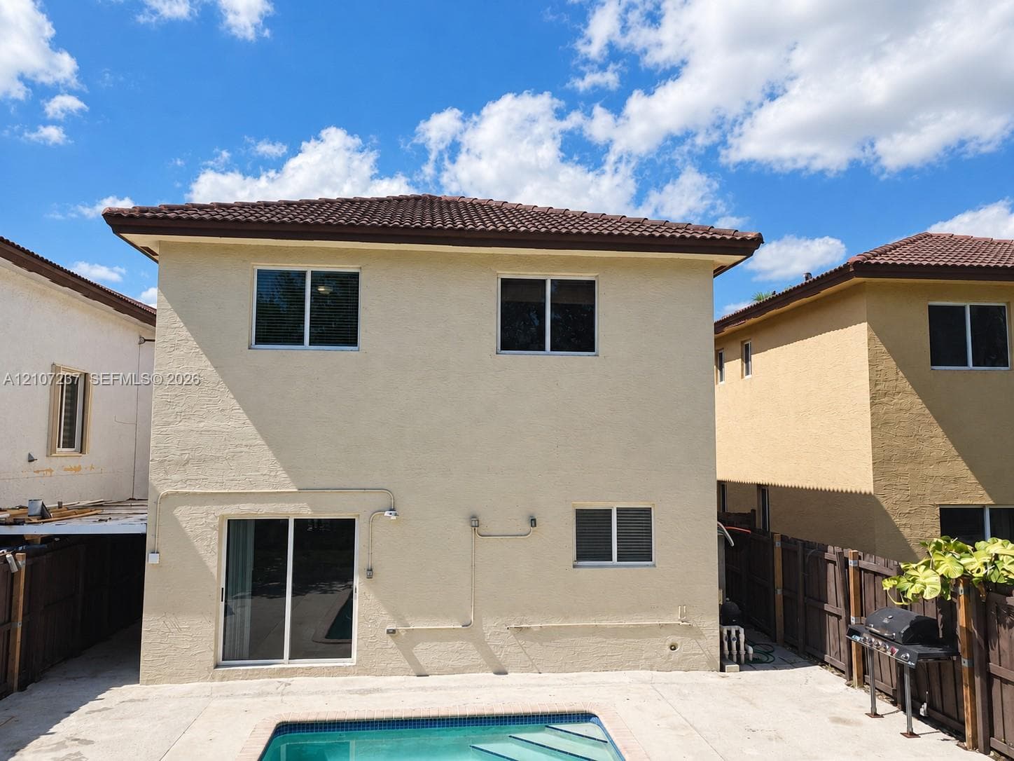 Two-story stucco exterior featuring a hipped tile roof, integrated sliding glass door, and an in-ground swimming pool with concrete decking