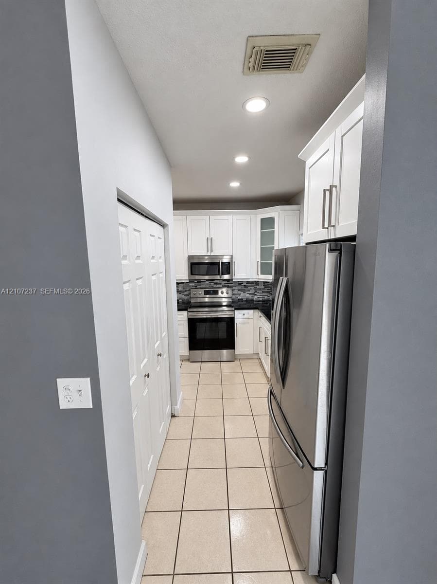 Kitchen featuring white shaker-style cabinetry, stainless steel appliances, tile flooring, and a multi-toned mosaic tile backsplash