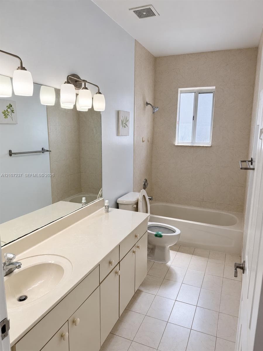 Bathroom featuring a large vanity with integrated countertop, wall-to-wall mirror, multi-light fixture, tile flooring, and a tiled tub-shower combination