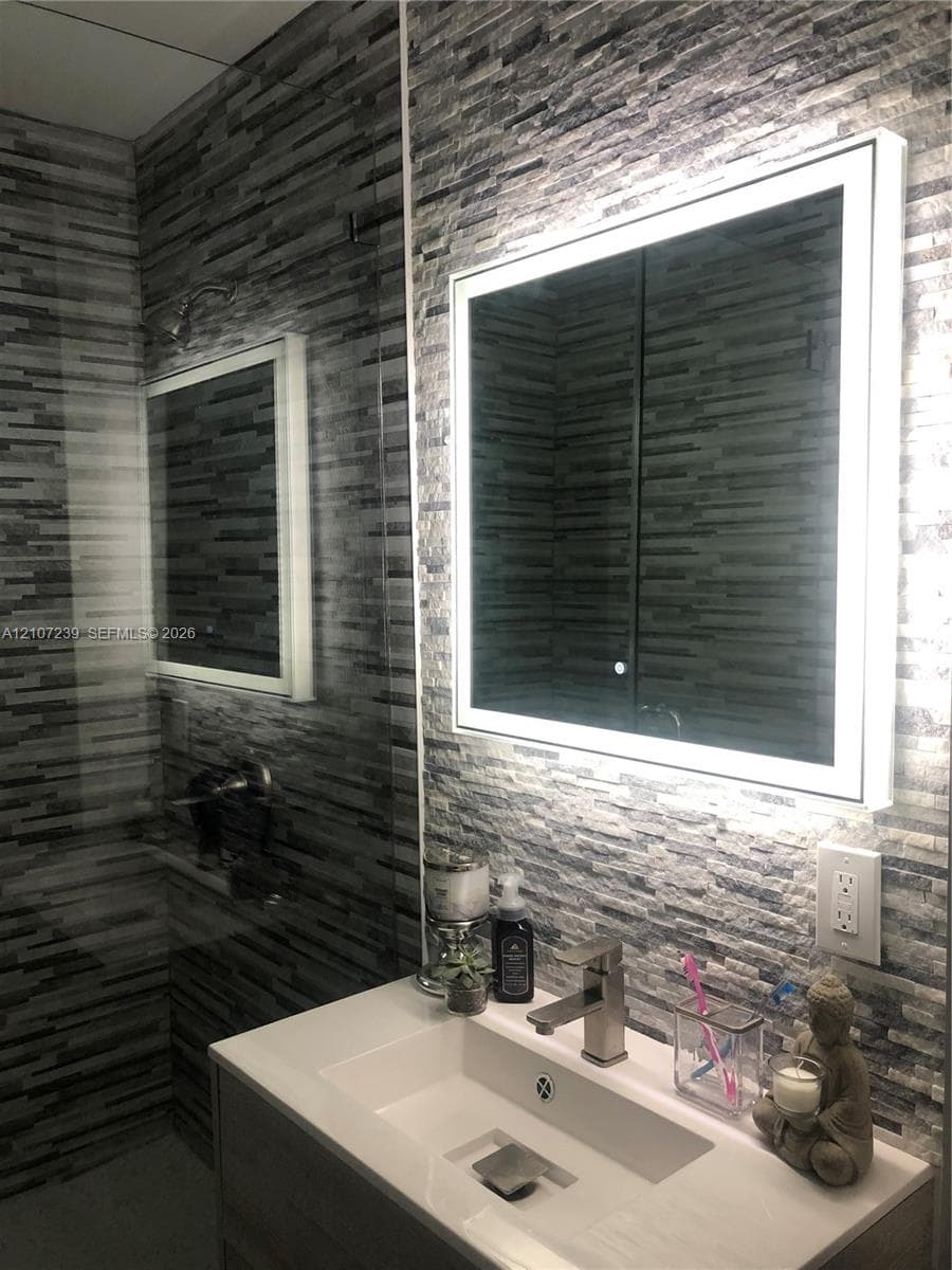 Modern vanity featuring a rectangular integrated sink, countertop, and a brushed-nickel faucet, complemented by a wall-mounted LED-backlit mirror and stacked-stone wall tiling