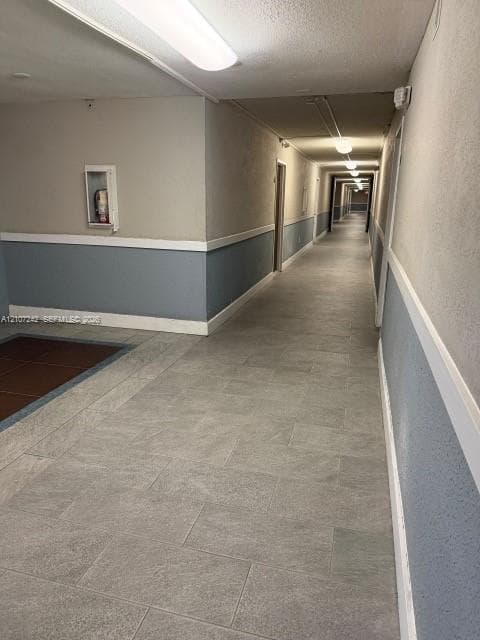 Hallway featuring light-toned stone-finish flooring, two-tone painted walls with chair rail trim, and flush-mount overhead lighting