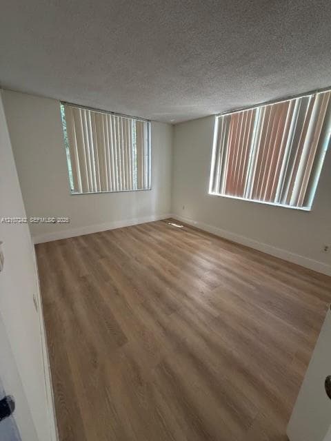 Interior room featuring wood-finish flooring, neutral wall tones, and two large windows with vertical blinds
