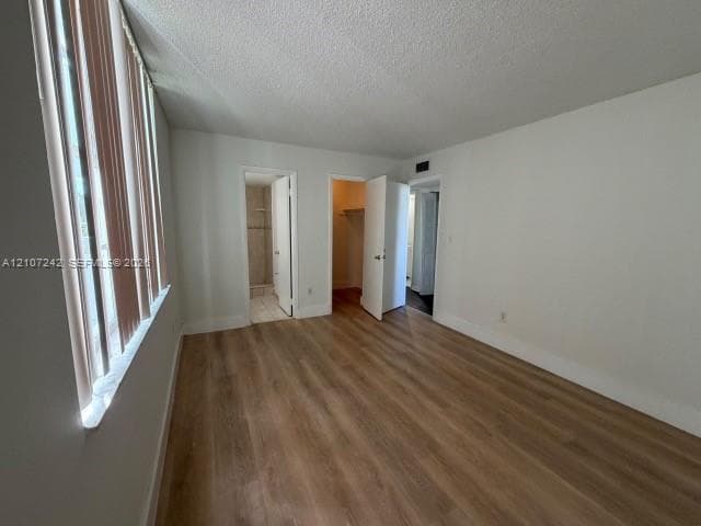 Wood-finish flooring, vertical window blinds, and reach-in closet with built-in shelving