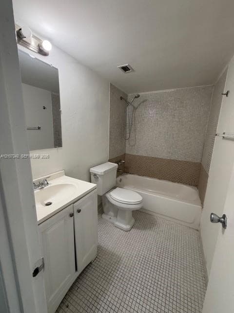 Bathroom featuring a white vanity cabinet with an integrated sink, a rectangular wall-mounted mirror, a two-piece toilet, and a bathtub with a tiled shower surround