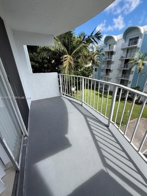 Covered balcony featuring a smooth-finish floor, white metal railing, and direct exposure to exterior greenery and landscaping