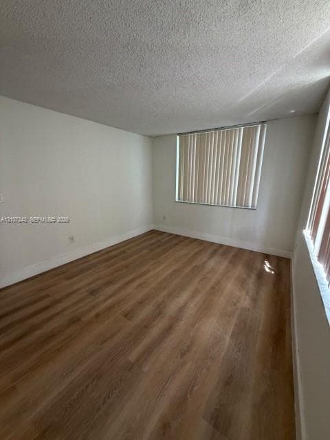 Neutral-toned interior room featuring wood-finish flooring, white walls, and vertical window blinds