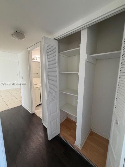 Storage closet featuring louvered bifold doors and built-in shelving, complemented by wood-finish flooring and a flush-mount ceiling light fixture