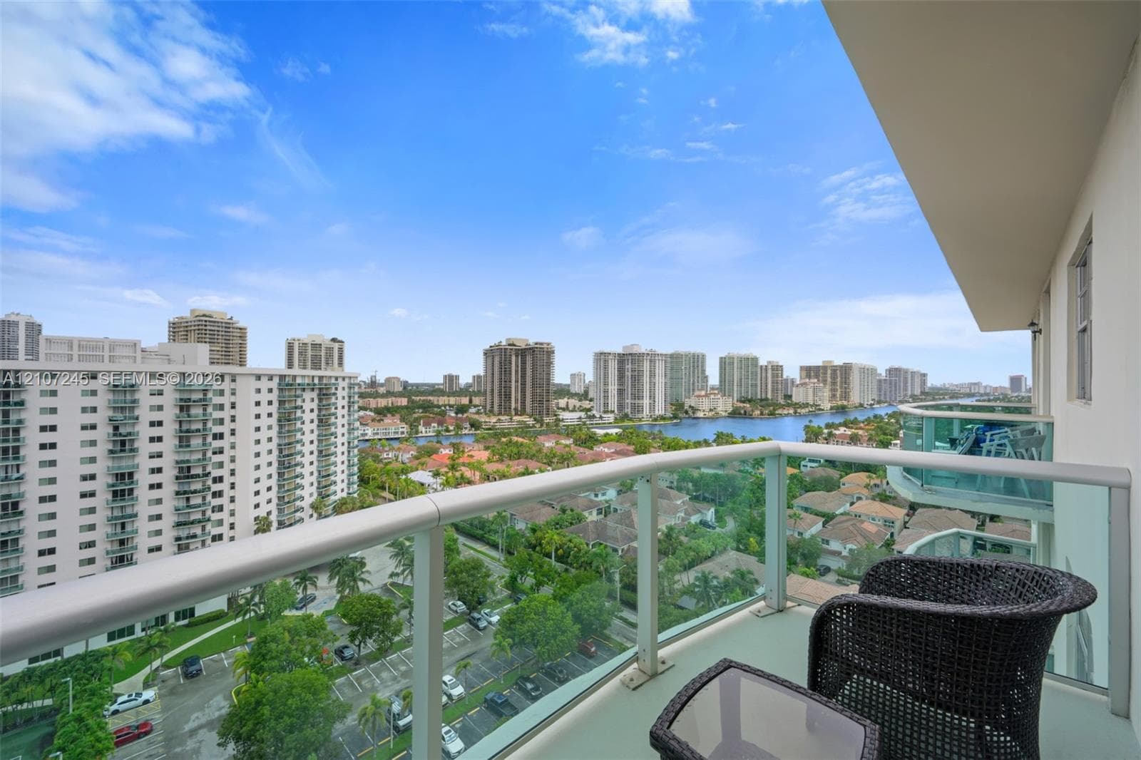 Private balcony featuring a glass panel railing and a metal handrail, offering an exterior perspective of the surrounding water and urban environment