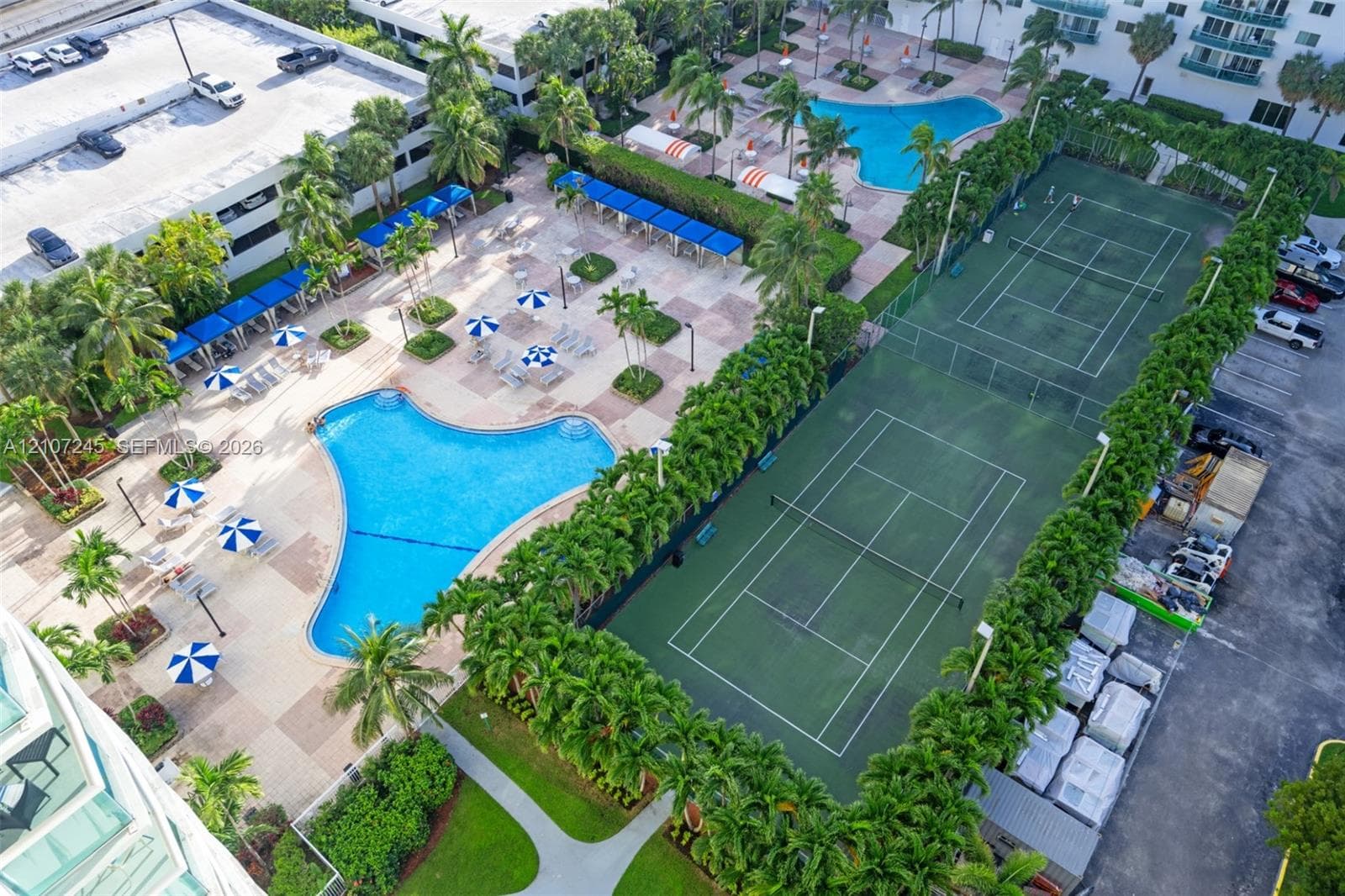 Recreational area featuring two fenced tennis courts, two swimming pools, paved pool decks, and mature landscaping