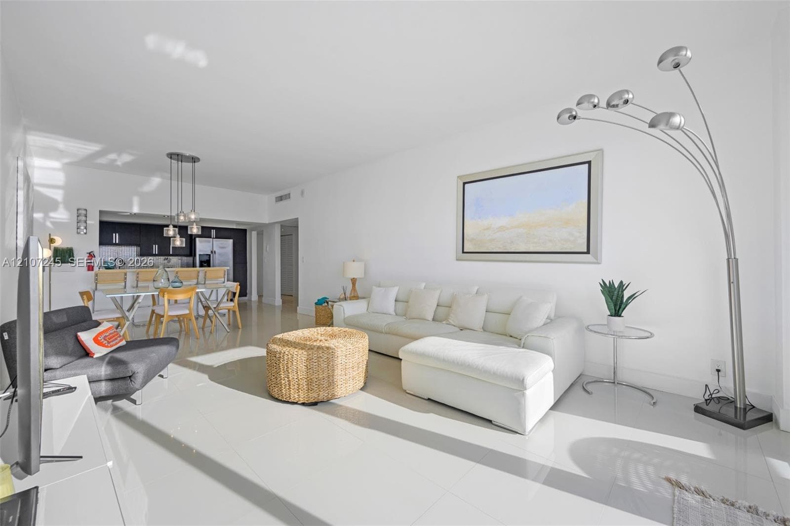 Open-concept interior featuring large-format tile flooring, recessed ceiling lighting, and a kitchen equipped with dark cabinetry, integrated bar seating, and multi-pendant lighting