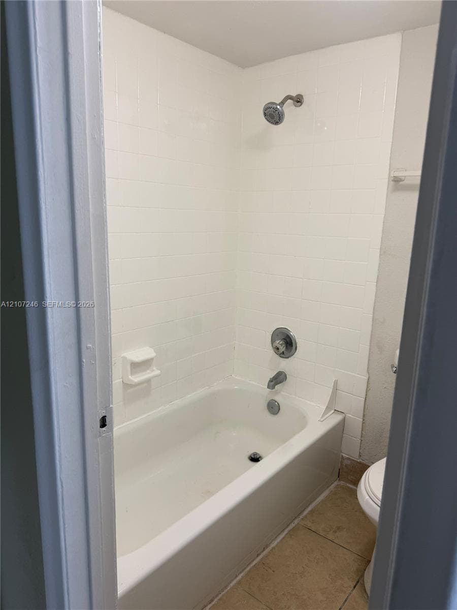 Full bathroom featuring a tub-shower combination with white subway-style tile surround, chrome plumbing fixtures, built-in soap dish, and tile flooring