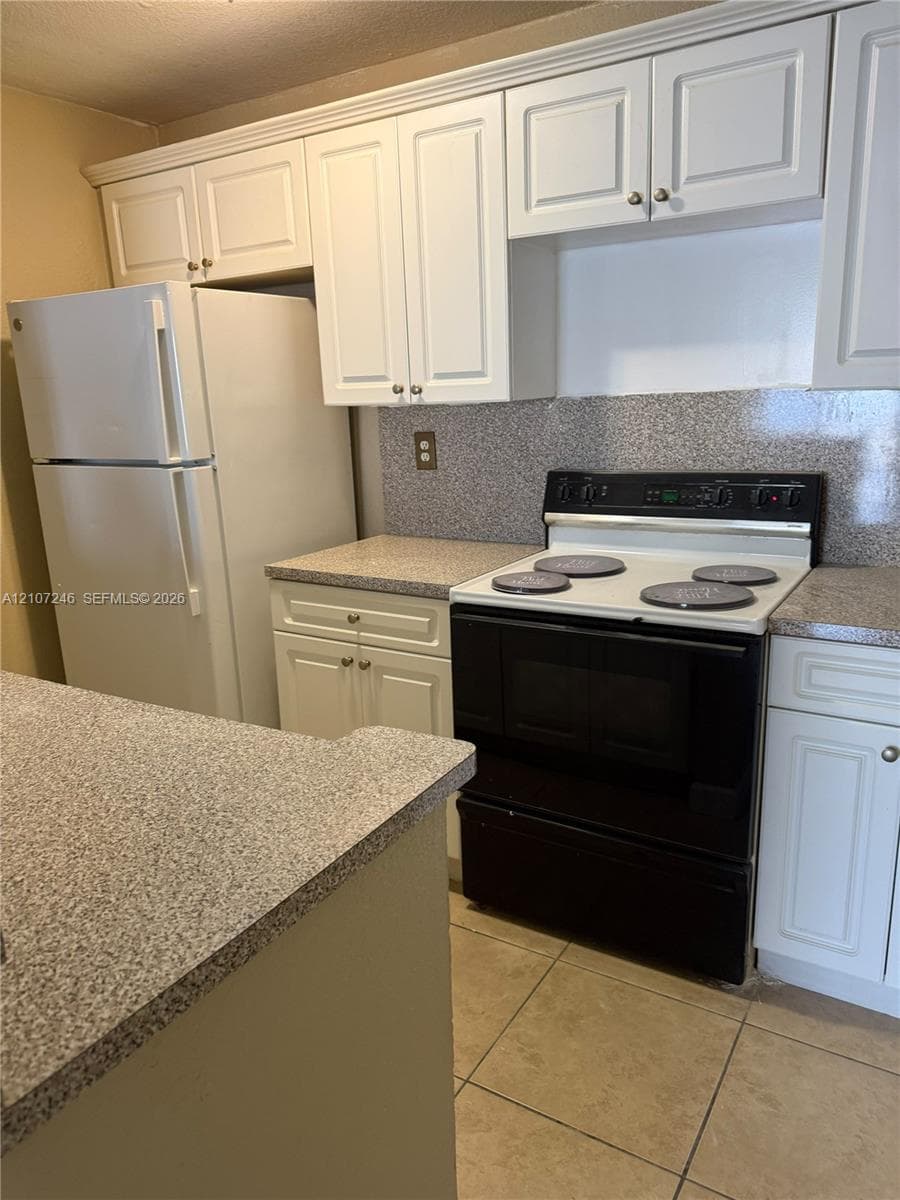 Kitchen featuring white shaker-style cabinetry, speckled stone-finish countertops, tile flooring, and a freestanding electric range