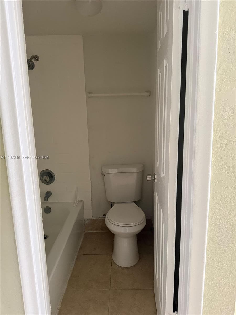 Bathroom featuring a tub-shower combination, wall-mounted faucet controls, standard-height toilet, tile flooring, and a towel bar