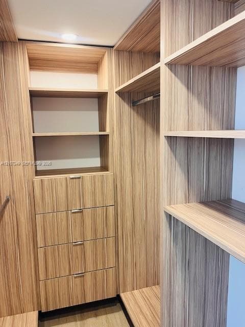 Custom wood-finish storage system featuring integrated shelving, four stacked drawers with metallic pulls, and a built-in clothing rod