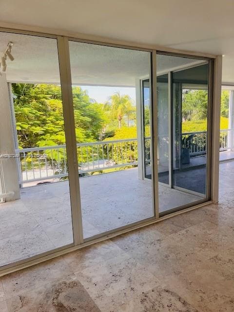 Large-format sliding glass doors with aluminum framing, stone tile flooring, and a covered balcony featuring a white metal railing