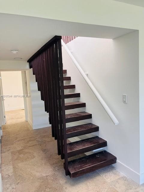 Open-tread staircase featuring dark wood-finish steps, a vertical slat balustrade, and a white wall-mounted handrail, set against stone flooring