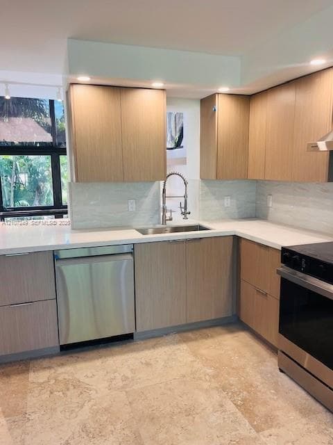 Kitchen featuring flat-panel wood-finish cabinetry, white countertops, textured tile backsplash, stainless steel appliances, and large-format stone flooring