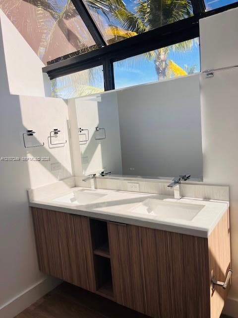 Floating wood-finish double vanity featuring a stone countertop, dual integrated sinks, chrome fixtures, and a glass-paneled ceiling feature
