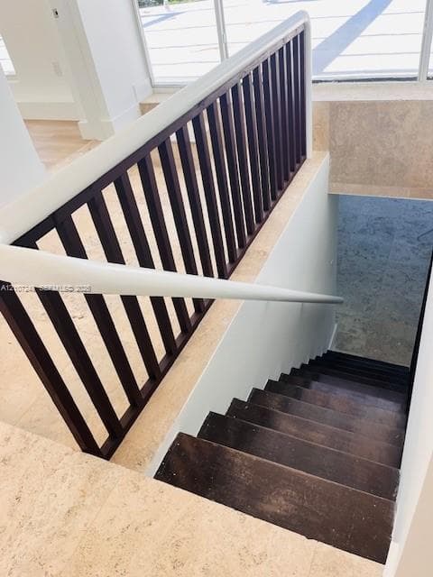 Staircase featuring dark-toned wood treads, stone-finish flooring, and a railing with a white handrail and dark-toned balusters
