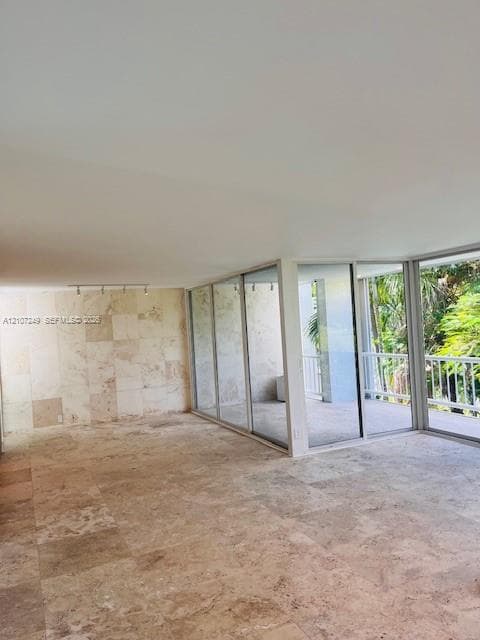 Interior space featuring large-format stone flooring, floor-to-ceiling stone wall cladding, expansive glass sliding doors, and track lighting