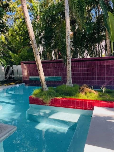 Swimming pool featuring an in-water landscaped island with mature palms, a tiled retaining wall with integrated water feature, and concrete steps