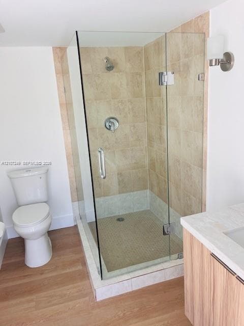 Walk-in shower featuring a frameless glass enclosure, tiled surround, and mosaic tile flooring, accompanied by wood-finish cabinetry, a neutral countertop, and wall-mounted lighting